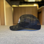 Black mesh cap with camouflage visor on a textured surface