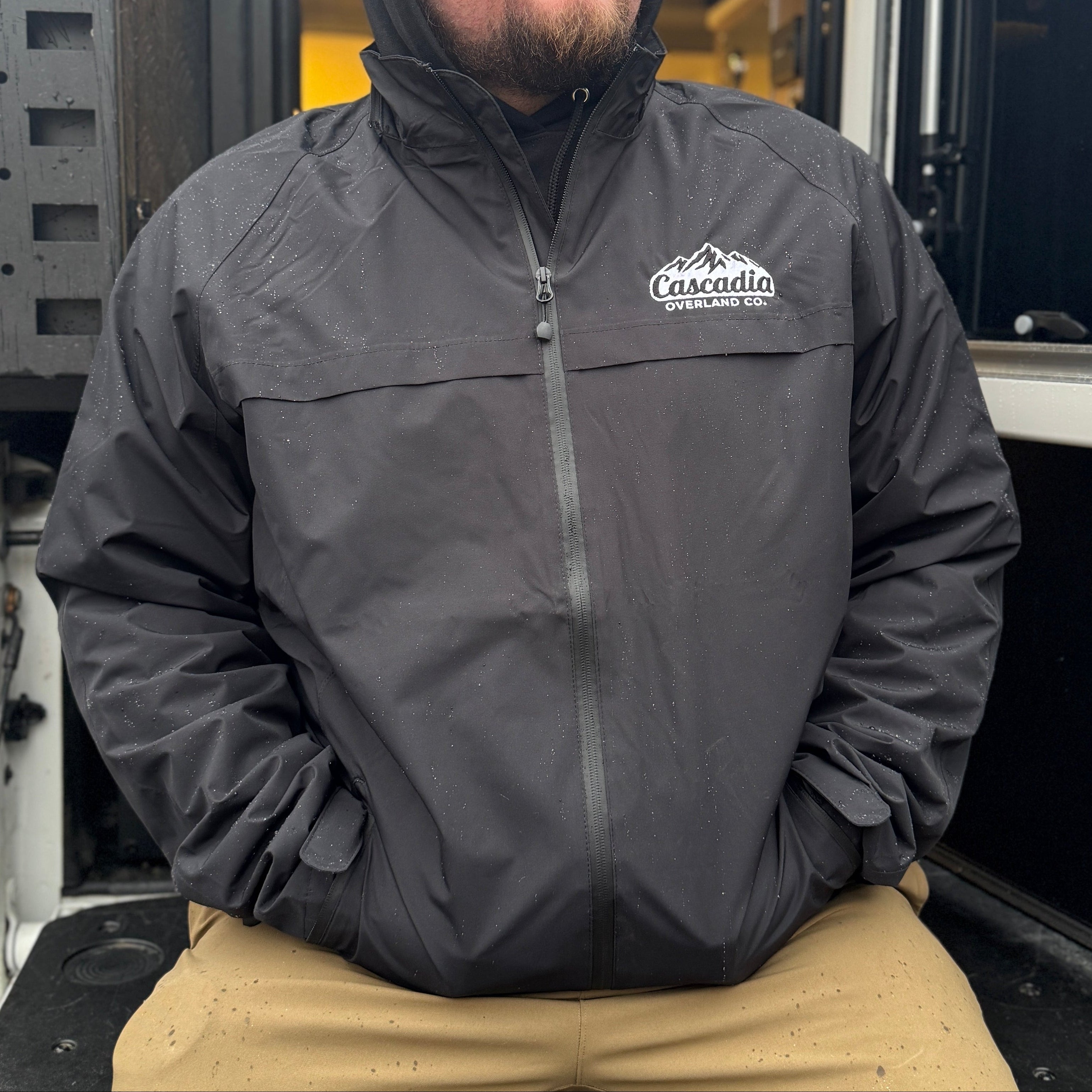 Man wearing a dark jacket with a logo, sitting in the back of a large vehicle.