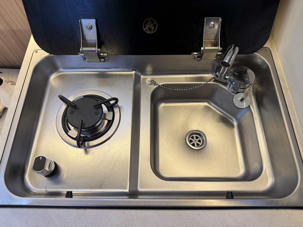 Stainless steel sink with gas stove inside a vehicle or RV.