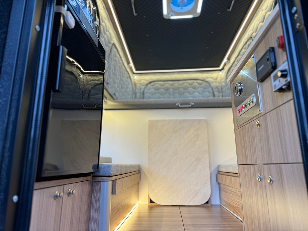 Luxury interior of a vehicle with wooden panels, a bed, and electronic controls.