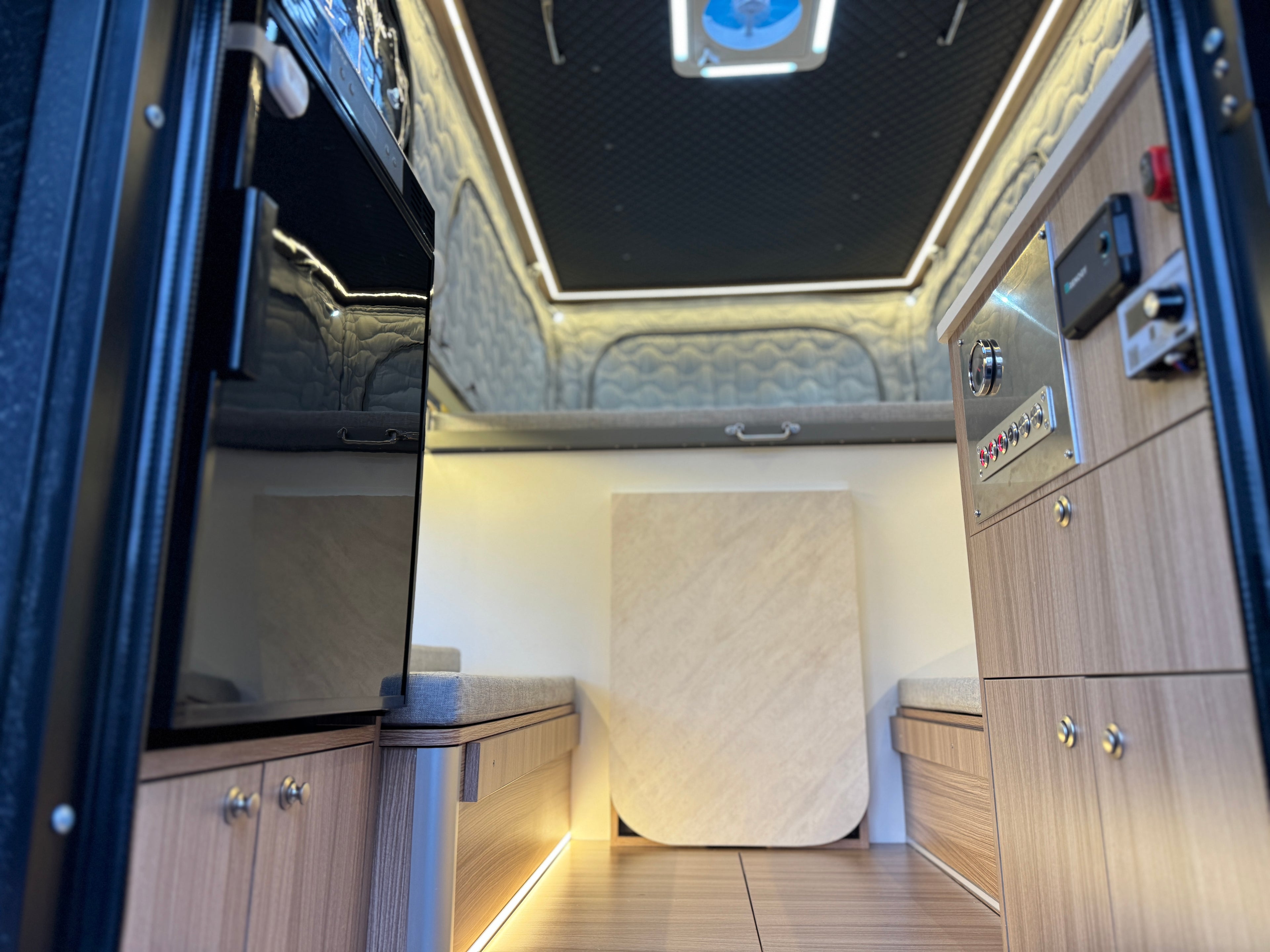 Luxury interior of a vehicle with wooden panels, a bed, and electronic controls.
