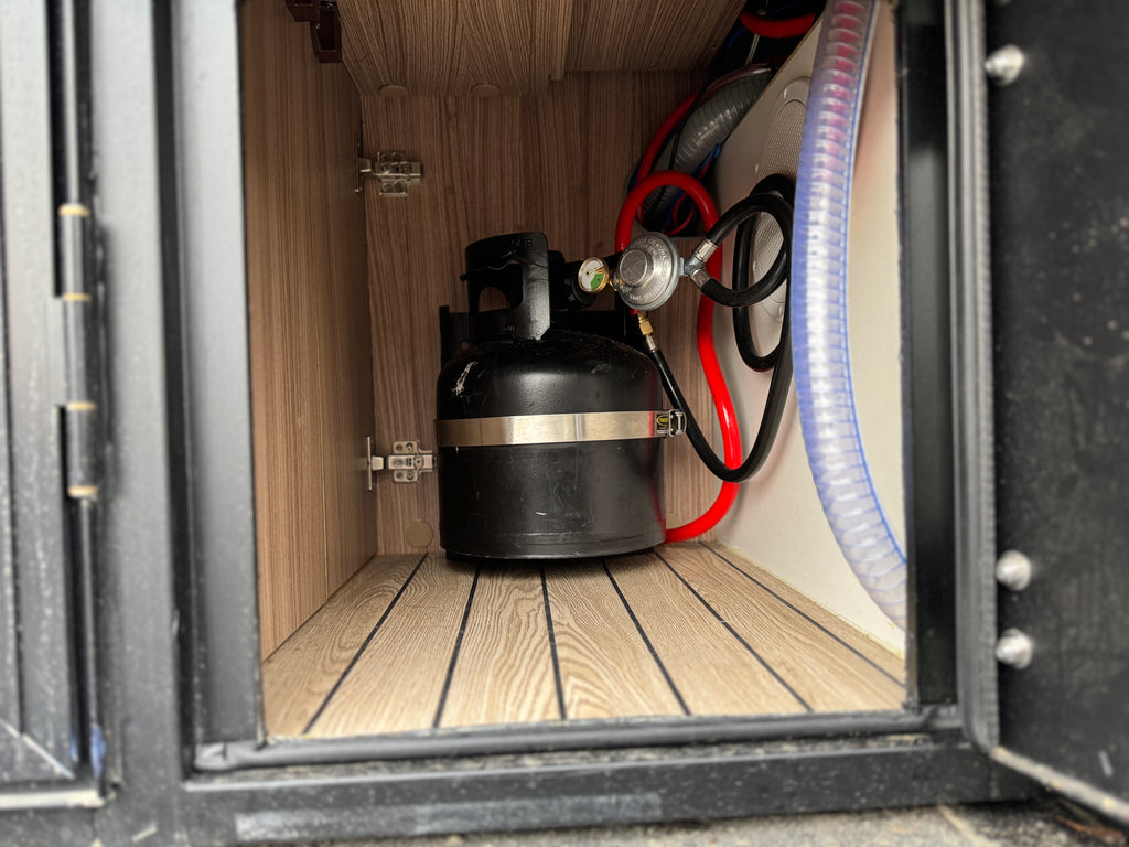 Propane tank inside a wooden cabinet with hoses and regulators.