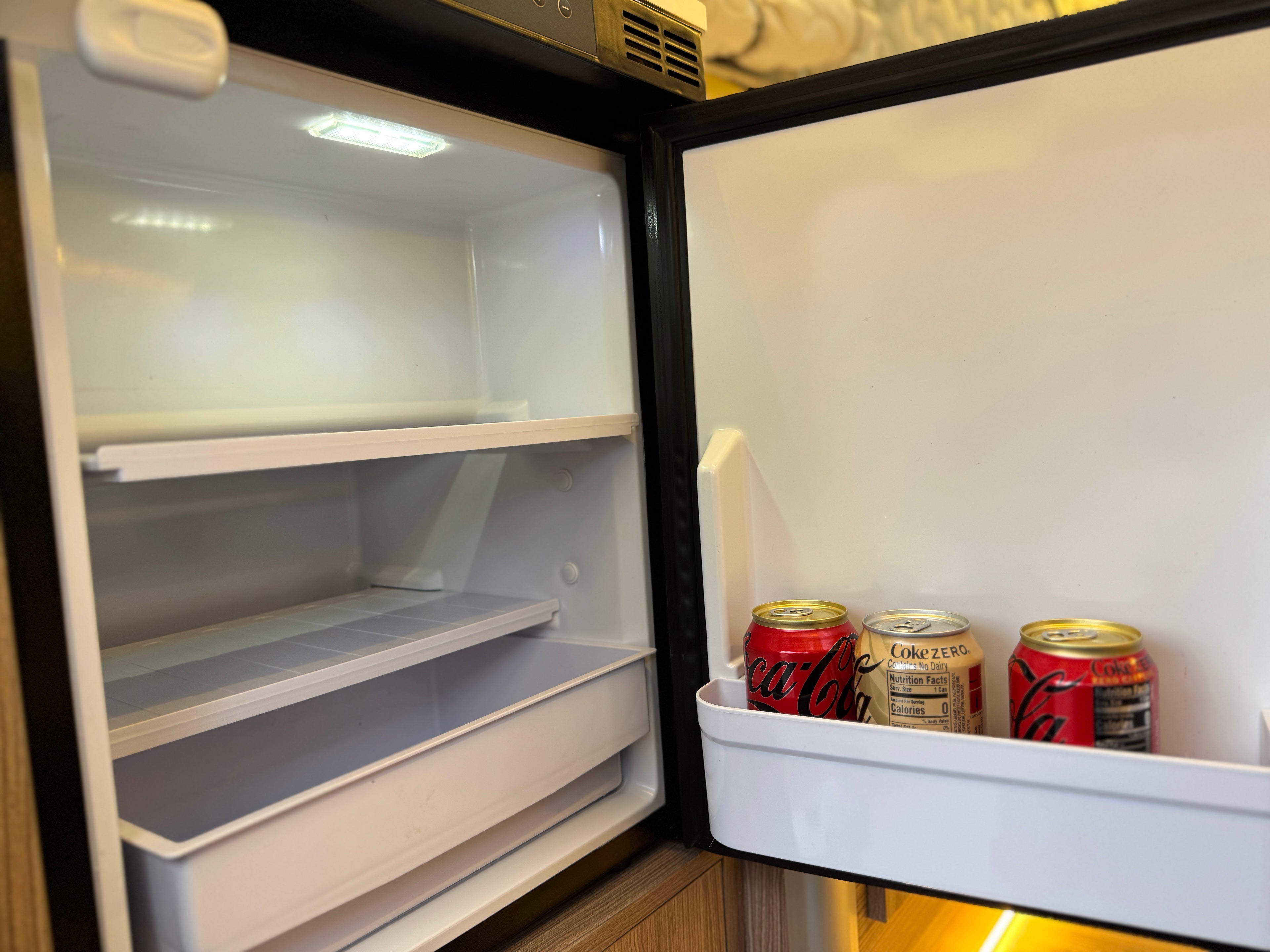 Open refrigerator with Coca-Cola cans inside the door.