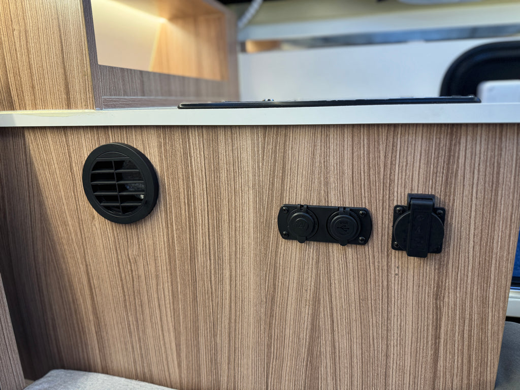 Wooden panel with black vent and outlets on a vehicle interior.