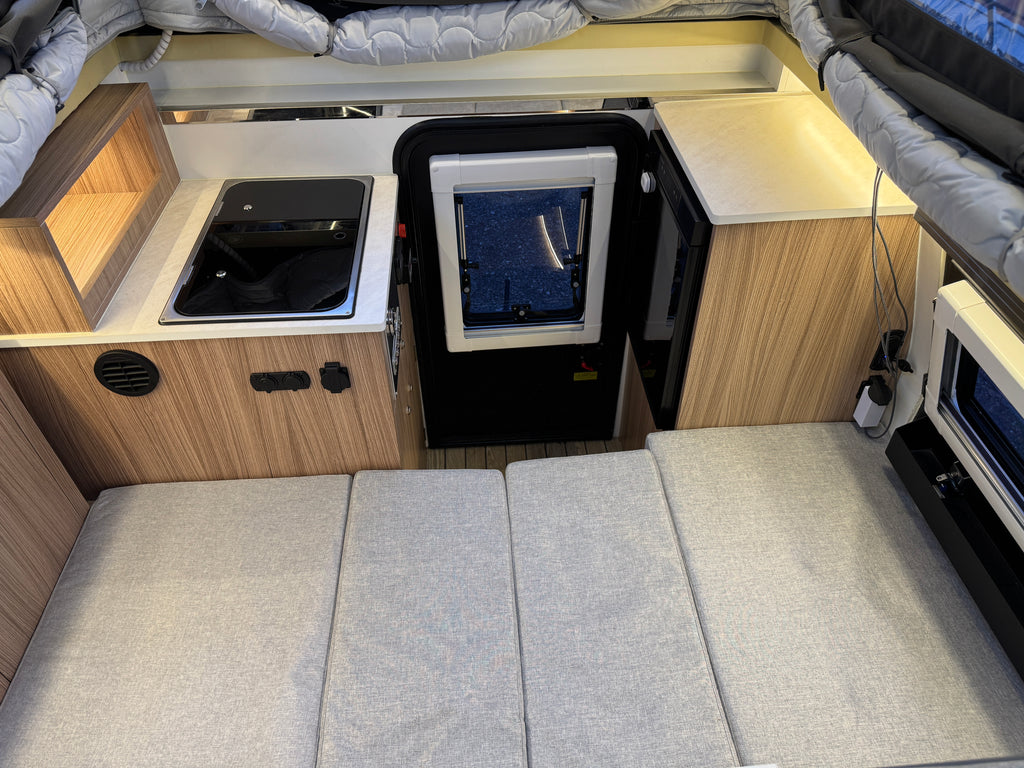 Compact kitchen area inside a vehicle with a stove, sink, and storage compartments.